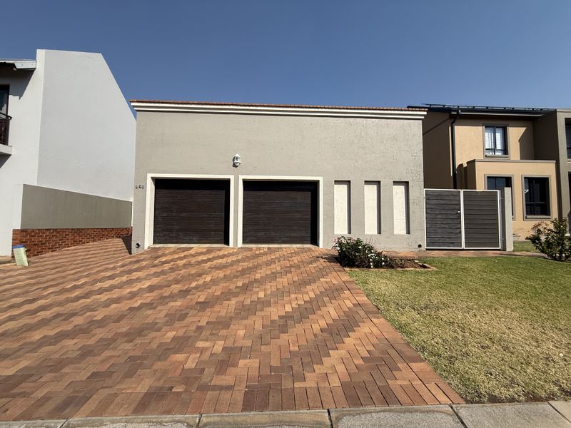 Front view of a modern house featuring a double garage with dark doors, a paved driveway, and a well-maintained lawn.