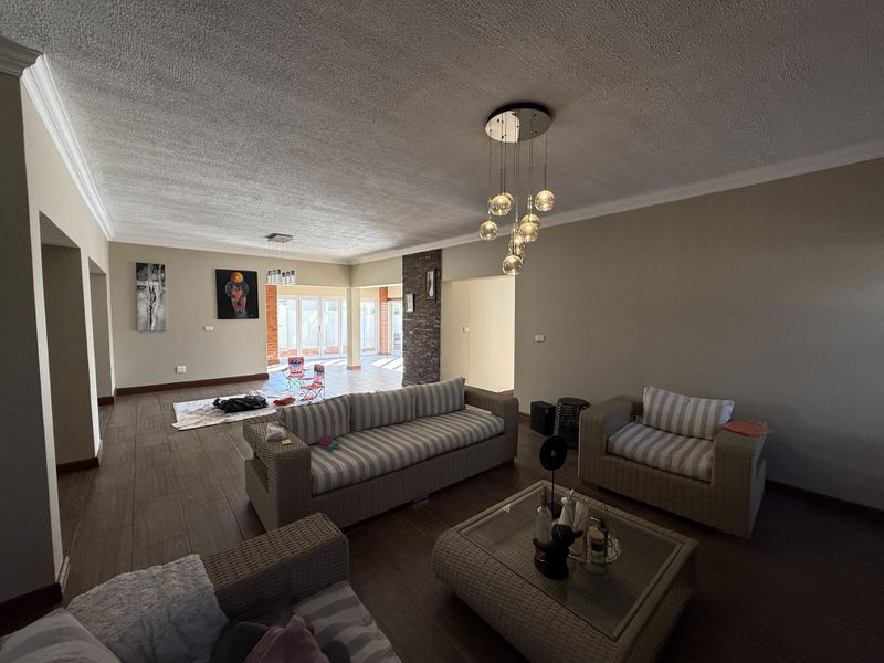 Spacious open-plan living area featuring tiled floors, a stone accent wall, and modern pendant lighting, leading to an adjacent sunroom or patio space.