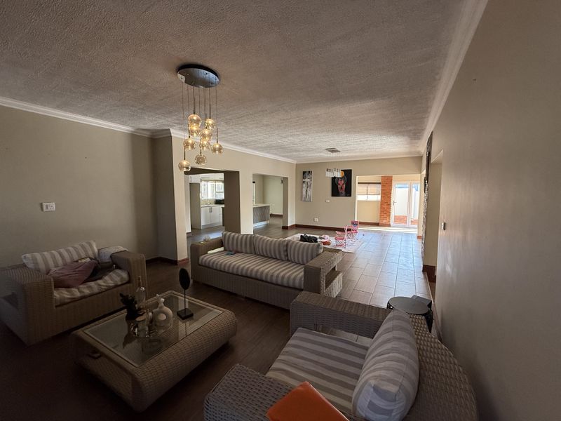 Spacious open-plan living area featuring tiled floors, coved cornicing, and modern pendant lighting, flowing seamlessly into the kitchen and outdoor access points.
