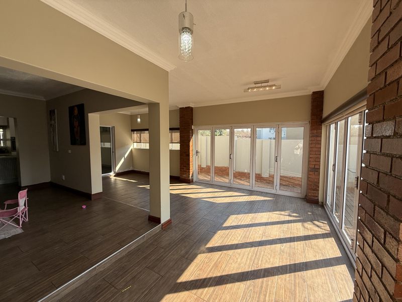 Spacious open-plan living area featuring wood-look tiled flooring, exposed brick pillars, and large folding glass doors providing abundant natural light and garden access.