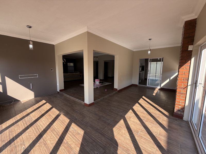 Spacious open-plan living area featuring wood-look tiled flooring, an exposed brick pillar, and sliding glass doors leading to the exterior.