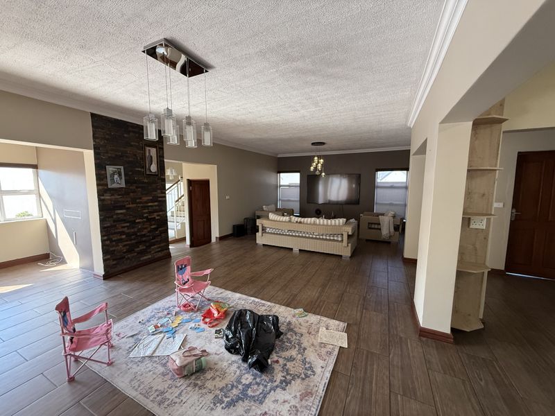 Spacious living room featuring a stone accent wall, tiled flooring, and modern pendant lighting, offering an open-plan layout with built-in shelving.