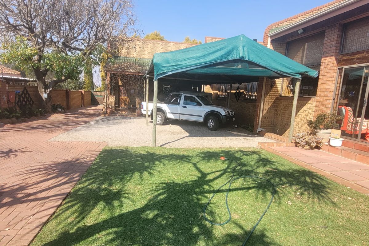 Rear exterior view featuring a brick-paved driveway, lawn area, and a covered patio space with sliding glass door access to the main house.