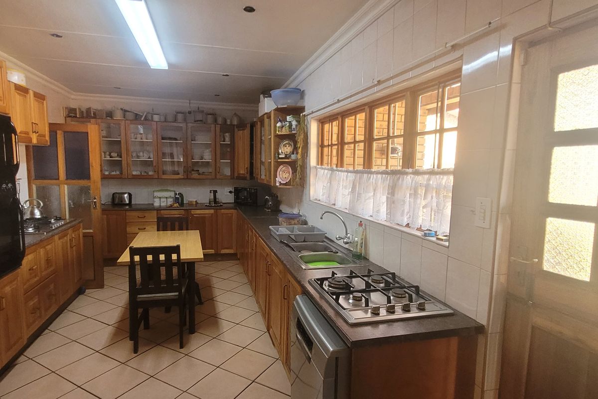 A functional kitchen featuring extensive wooden cabinetry, a gas hob, built-in oven, double sink, and tiled finishes throughout.