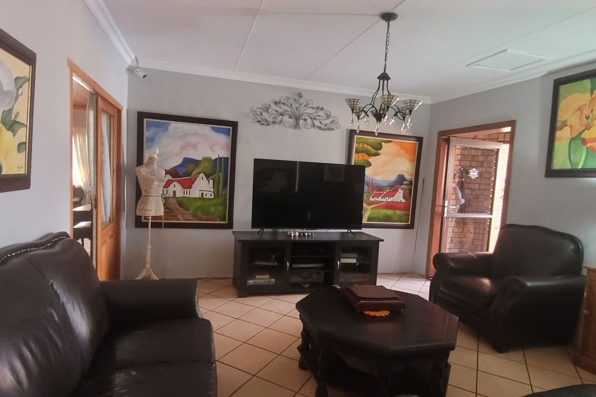 A comfortable living room featuring tiled flooring, cove cornicing, and a central chandelier, providing a functional and well-maintained space for relaxation.