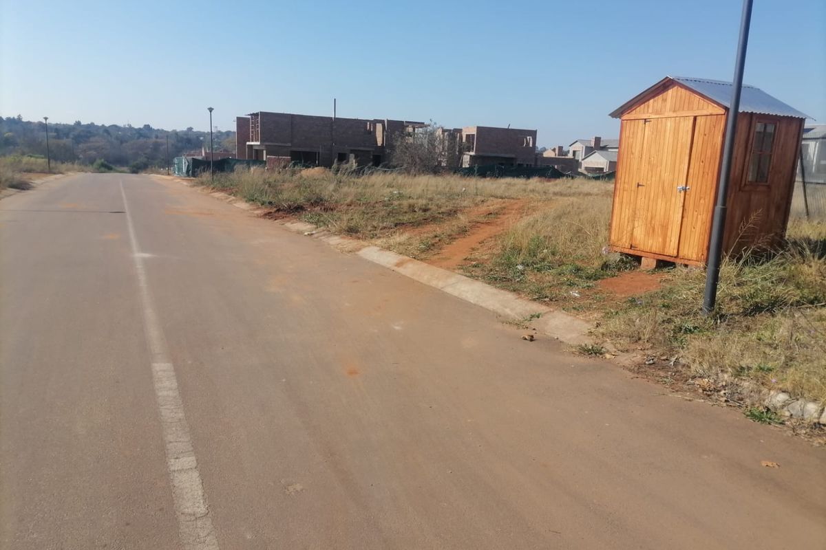 A street view of a vacant residential plot featuring a small wooden shed, adjacent to ongoing construction in a developing neighborhood.