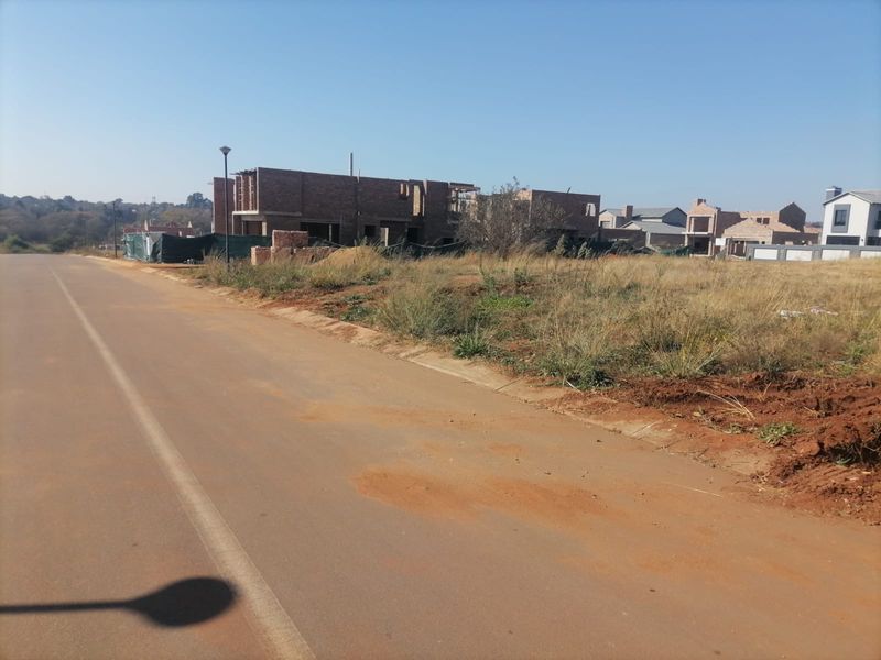 A street-level view of a vacant residential plot in a developing estate with surrounding construction activity.