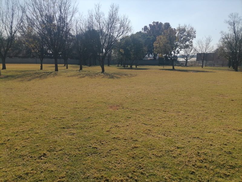 A spacious, level residential plot featuring a well-maintained grass lawn and several mature trees, offering a clear area for potential development.