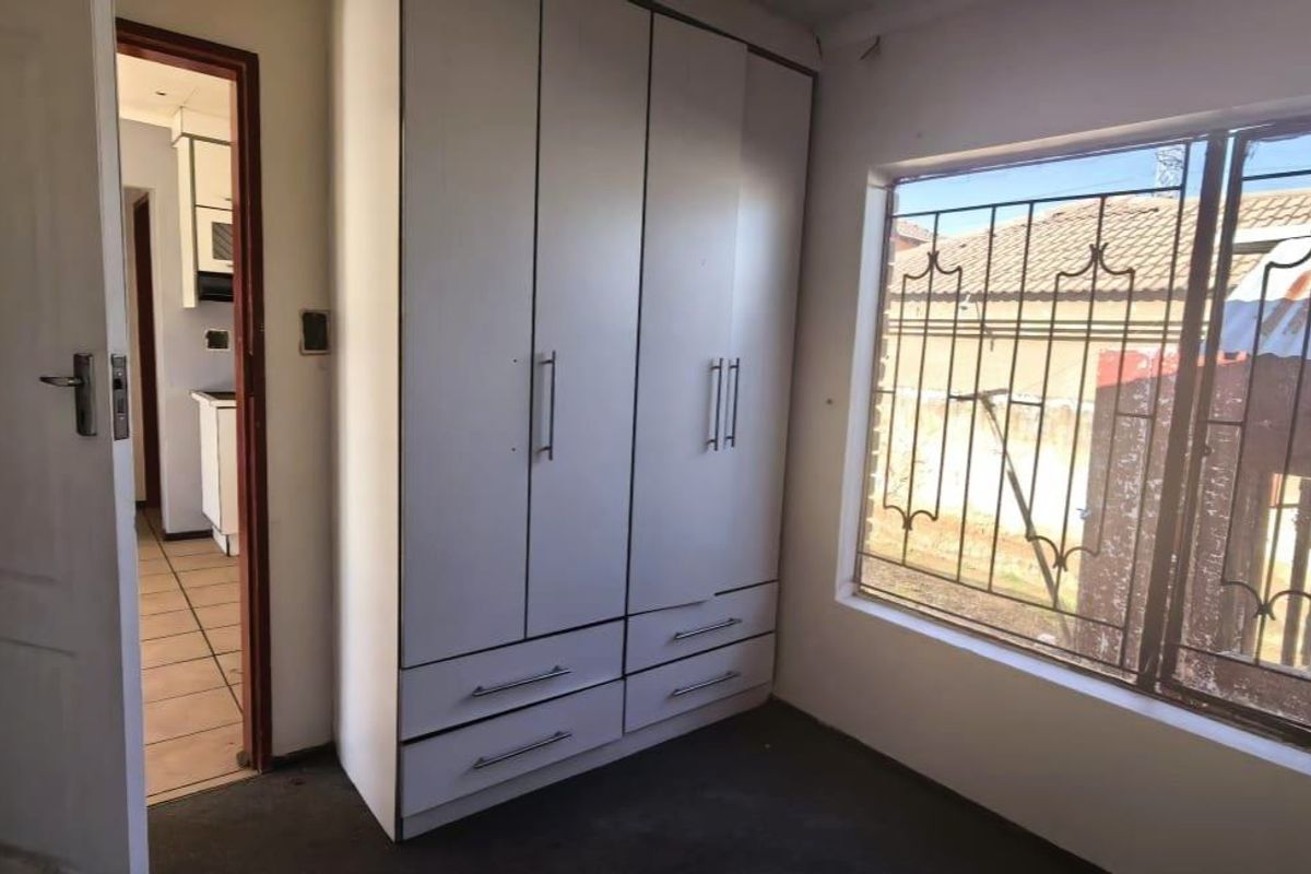 A bedroom featuring a built-in wardrobe, security bars on the window, and direct access to the hallway.