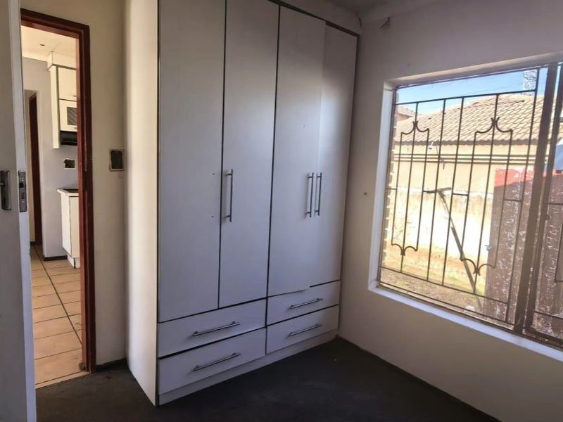 A bedroom featuring a built-in wardrobe, security bars on the window, and direct access to the hallway.