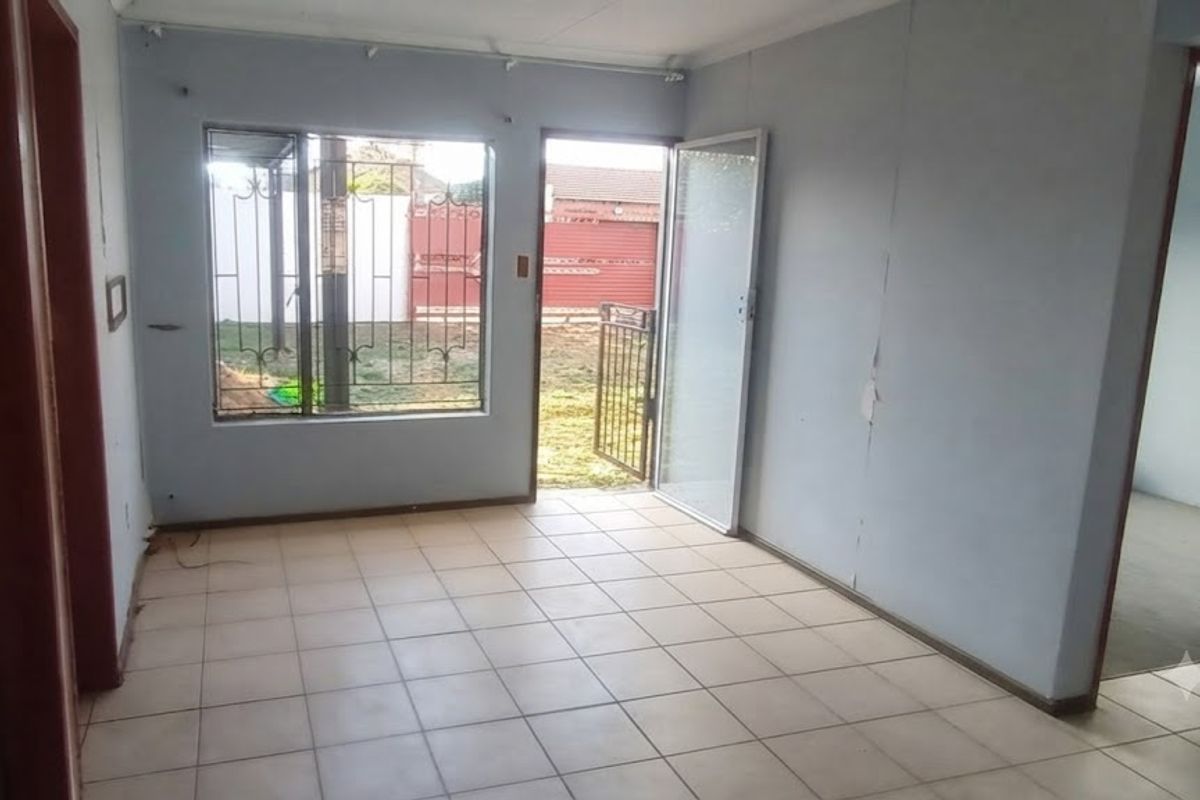 An empty living room featuring tiled flooring, security gate access to the exterior, and window security bars, requiring minor cosmetic wall repairs.