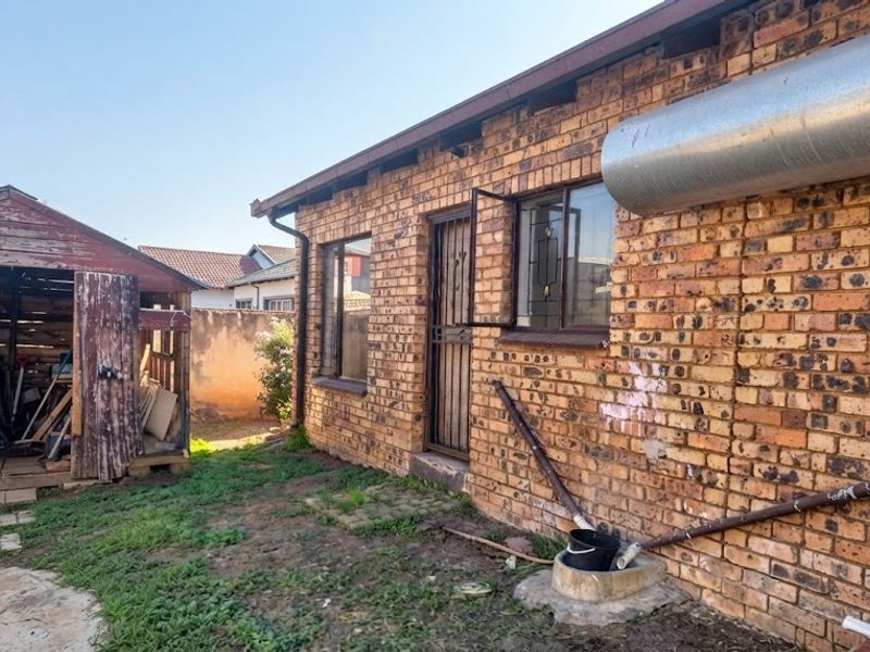 Rear exterior view of a face brick house featuring a weathered timber garden shed and exposed external utility piping.