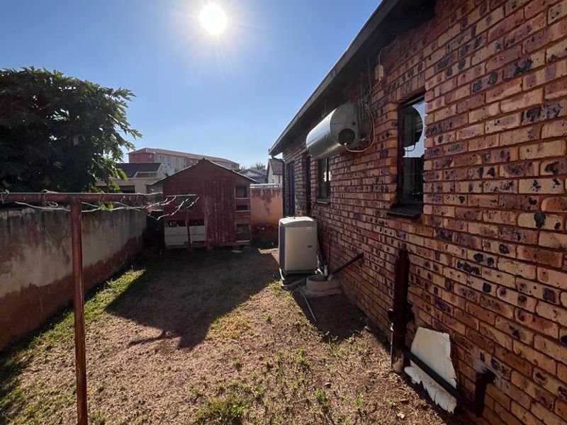 Rear exterior view of the property featuring a brick facade, external geyser, air conditioning unit, and a small garden area with a storage shed.