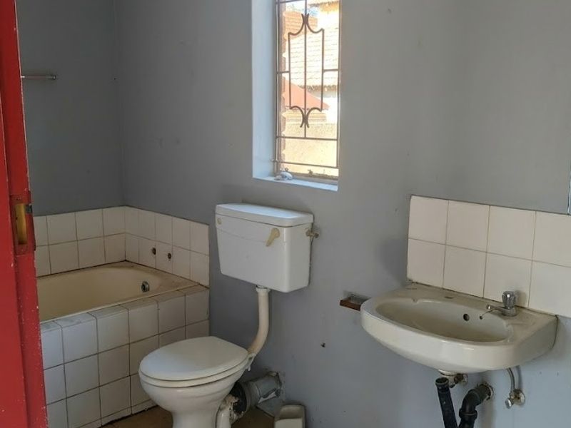 A functional bathroom featuring a built-in bathtub, wall-mounted basin, and toilet, with ceramic tile flooring and security bars on the window.