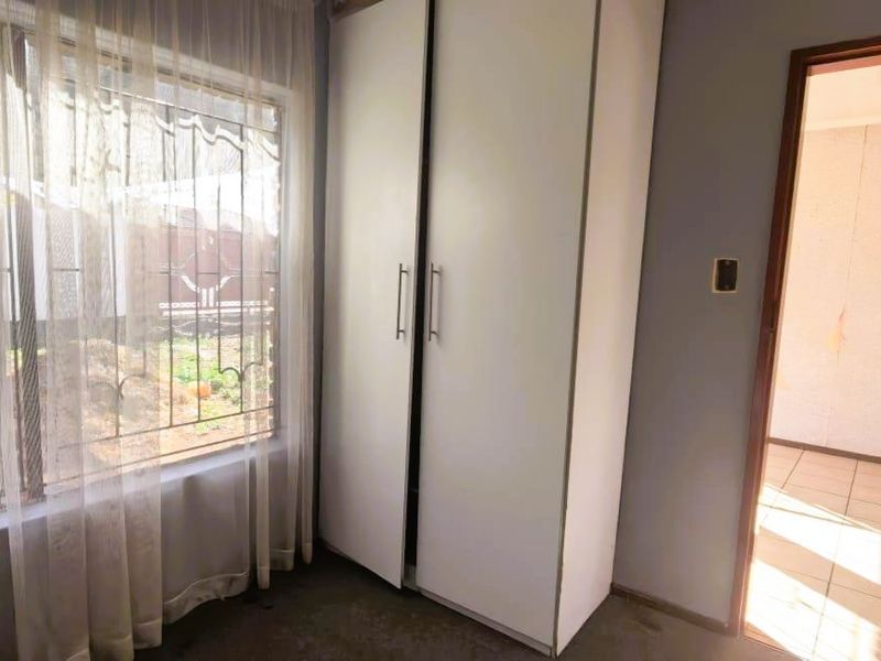 A bedroom featuring a built-in wardrobe, security bars on the window, and tiled flooring in the adjacent hallway.