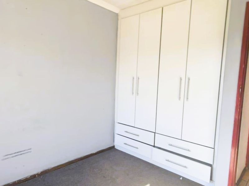 A vacant bedroom featuring built-in white wardrobes and carpeted flooring, requiring minor cosmetic updates to refresh the space.