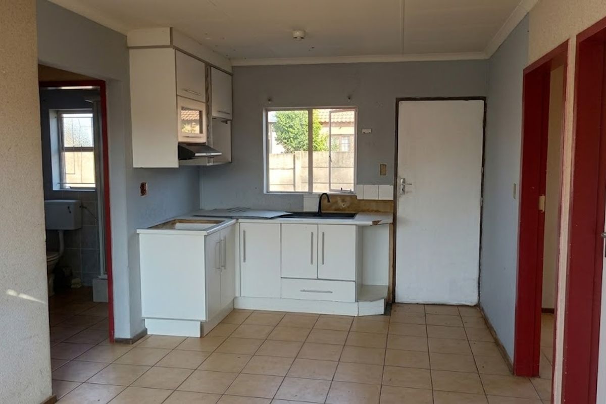 A compact kitchen featuring white cabinetry, tiled flooring, and an integrated extractor fan, currently in need of cosmetic updates and countertop repairs.
