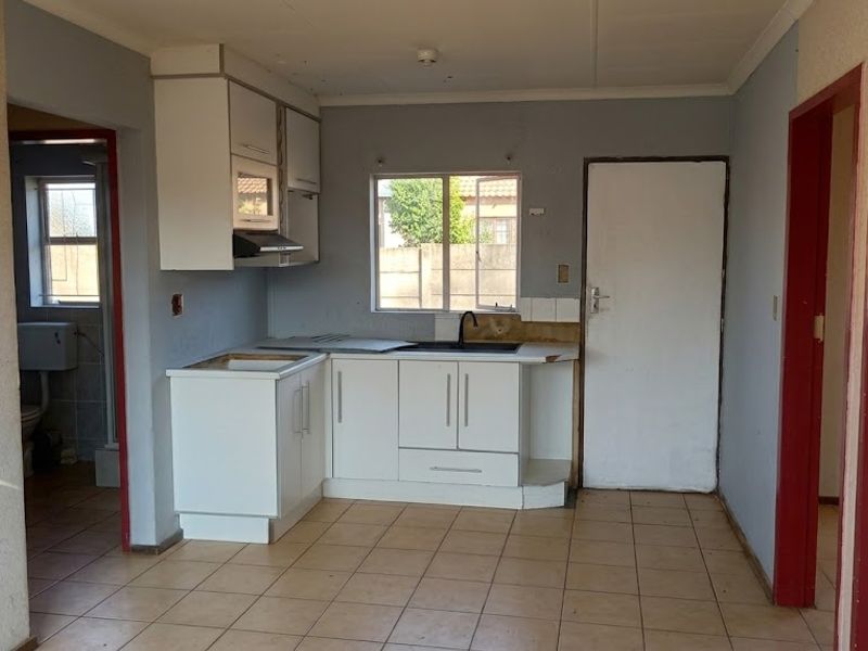 A compact kitchen featuring white cabinetry, tiled flooring, and an integrated extractor fan, currently in need of cosmetic updates and countertop repairs.