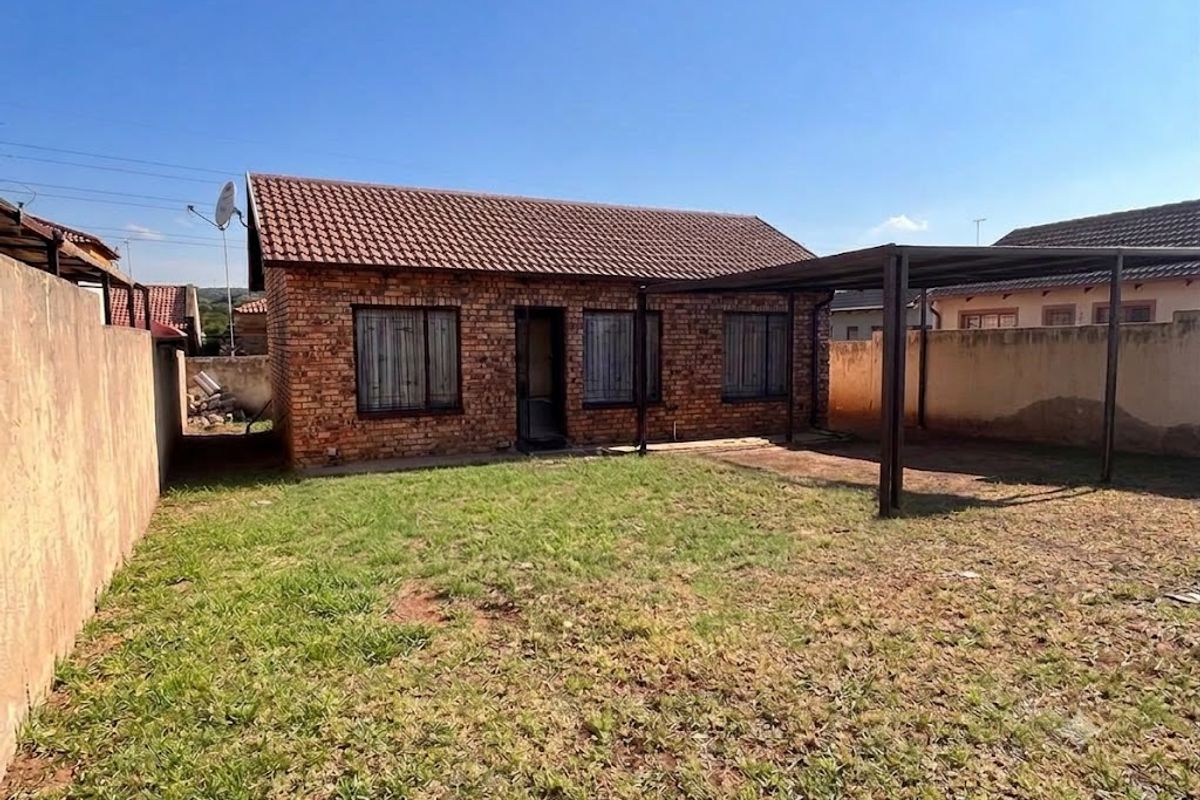 Rear view of a face brick house featuring a tiled roof, a covered carport area, and a private backyard with a boundary wall.
