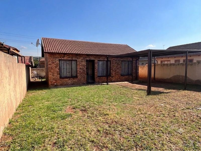 Rear view of a face brick house featuring a tiled roof, a covered carport area, and a private backyard with a boundary wall.