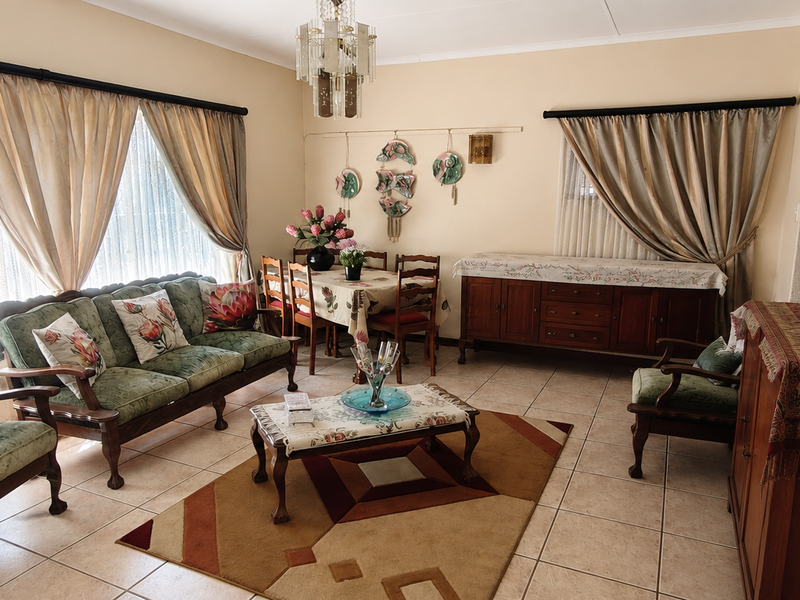 A spacious living room featuring neutral wall tones, ceramic floor tiles, and a classic crystal chandelier, offering a comfortable and traditional living environment.