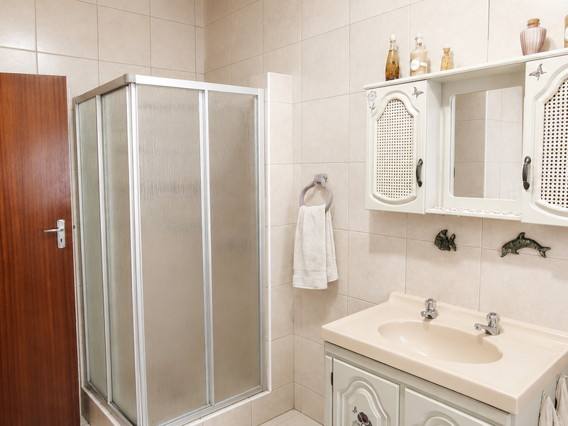 A functional bathroom featuring a corner shower enclosure, a vanity unit with integrated basin, and a wall-mounted storage cabinet with mirror.