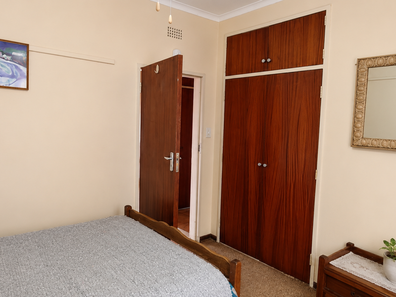 A bedroom featuring built-in wooden wardrobes, carpeted flooring, and neutral wall finishes, offering a functional space with classic storage solutions.