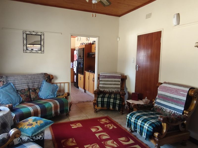 A living room featuring tiled flooring and a timber ceiling, with an open doorway leading through to the kitchen area.