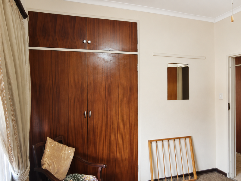 A bedroom featuring a large built-in wooden wardrobe, neutral wall finishes, and a standard internal door leading to an adjacent space.
