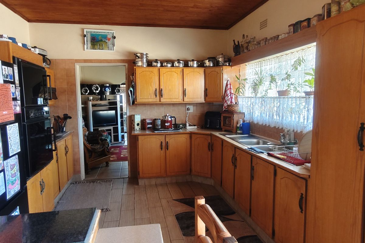 A functional kitchen featuring wooden cabinetry, tiled flooring, a double basin sink, and a warm wooden ceiling, offering a traditional aesthetic.
