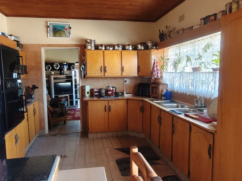 A functional kitchen featuring wooden cabinetry, tiled flooring, a double basin sink, and a warm wooden ceiling, offering a traditional aesthetic.