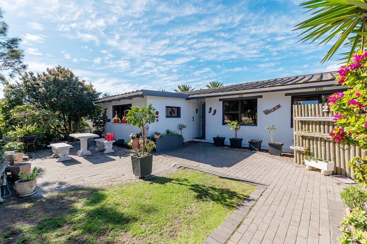 A well-maintained rear exterior view featuring a paved patio area, established garden, and a single-story dwelling with tiled roofing and aluminium window frames.