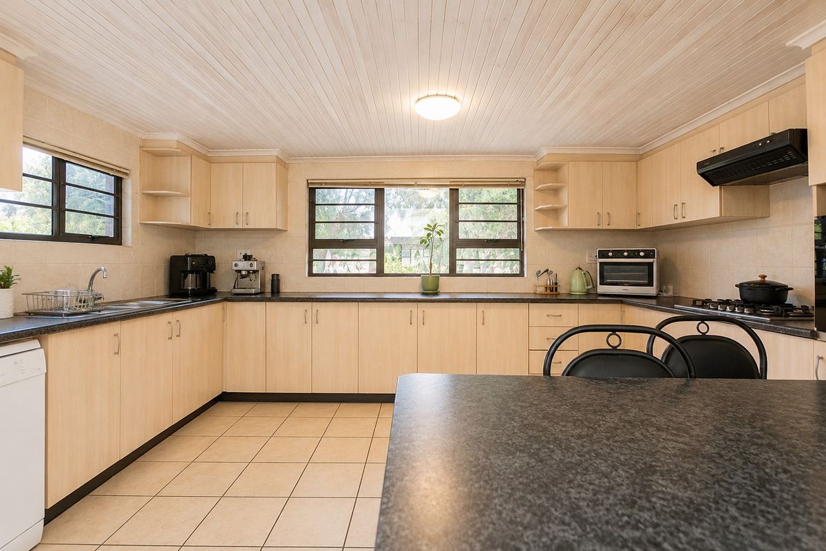 A functional kitchen featuring light wood-finish cabinetry, dark countertops, tiled flooring, and a tongue and groove ceiling with integrated appliances.