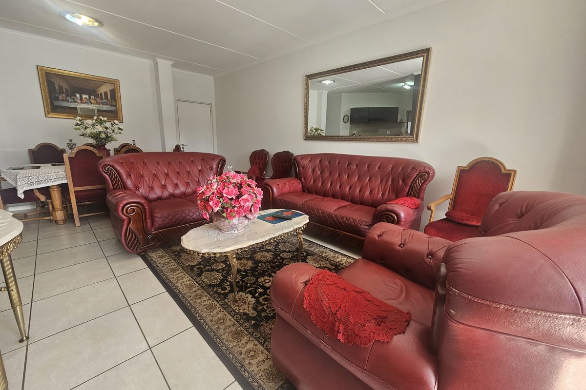A spacious living room featuring neutral tiled flooring and recessed ceiling lighting, providing a functional base for a comfortable seating area.