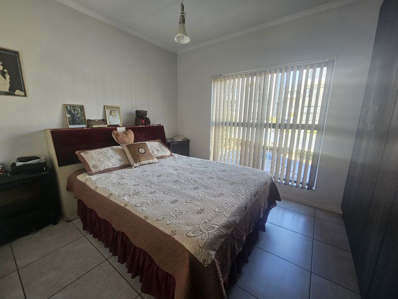 A bedroom featuring tiled flooring, built-in wardrobe storage, and vertical window blinds, offering a functional space with neutral wall finishes.