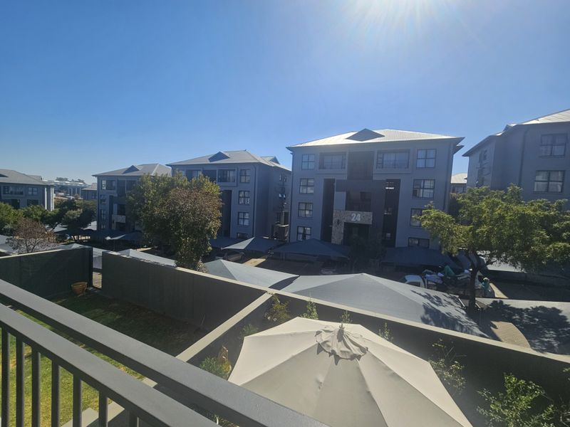Elevated view overlooking the townhouse complex, featuring modern multi-story residential buildings, paved parking areas with carports, and landscaped grounds.