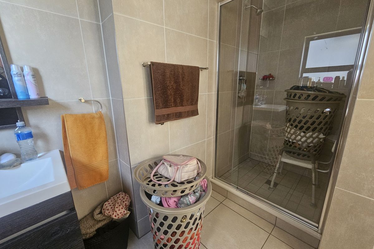 A functional bathroom featuring a glass-enclosed shower, vanity cabinet, and neutral ceramic tiling throughout.