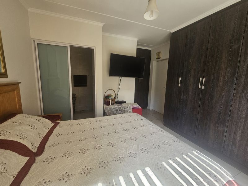 A bedroom featuring dark wood built-in cupboards, tiled flooring, and direct access to an en-suite bathroom.