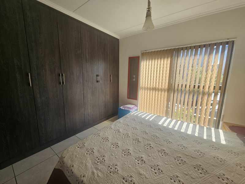 A well-maintained bedroom featuring dark wood built-in cupboards, tiled flooring, and vertical blinds allowing natural light.