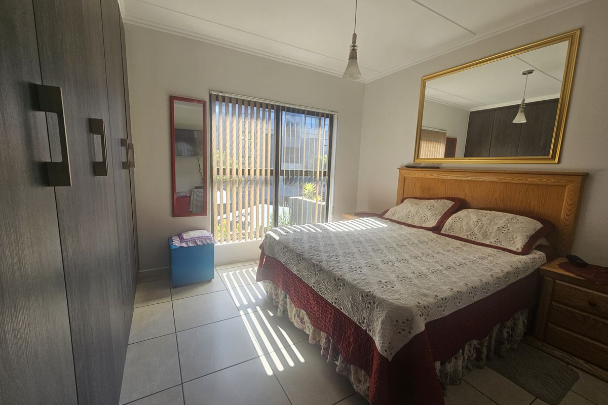 A bedroom featuring built-in cupboards, tiled flooring, and a sliding door with vertical blinds, providing access to the exterior.