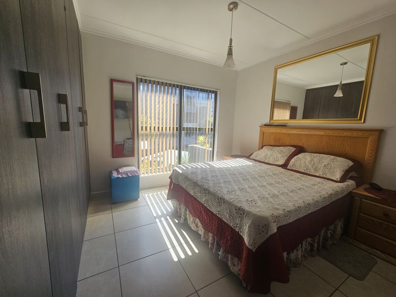 A bedroom featuring built-in cupboards, tiled flooring, and a sliding door with vertical blinds, providing access to the exterior.