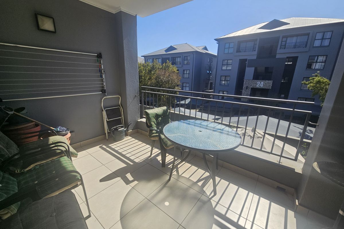 A covered balcony featuring tiled flooring, a metal safety railing, and a wall-mounted drying rack, offering an open view of the surrounding complex.