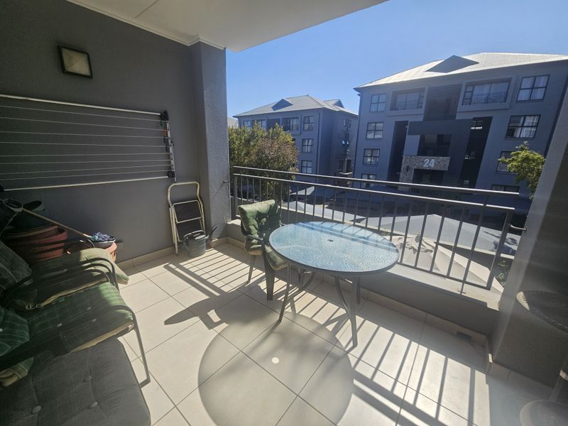 A covered balcony featuring tiled flooring, a metal safety railing, and a wall-mounted drying rack, offering an open view of the surrounding complex.