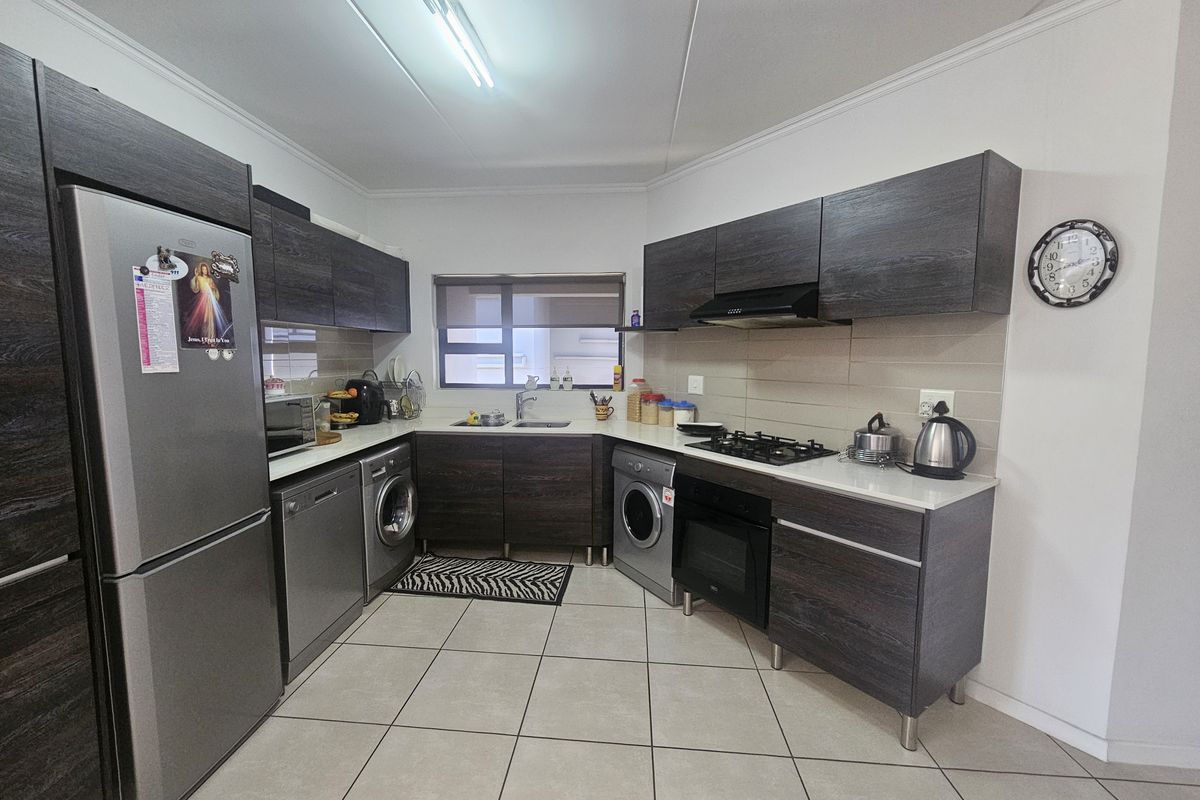 Modern kitchen featuring dark wood cabinetry, stone countertops, built-in oven, gas hob, extractor fan, and tiled flooring.