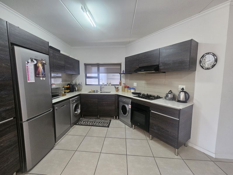 Modern kitchen featuring dark wood cabinetry, stone countertops, built-in oven, gas hob, extractor fan, and tiled flooring.