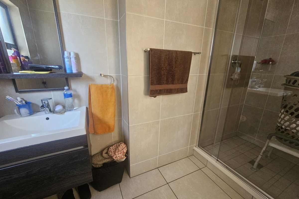 A functional bathroom featuring a modern vanity cabinet, ceramic basin, and a glass-enclosed shower with neutral wall and floor tiling.