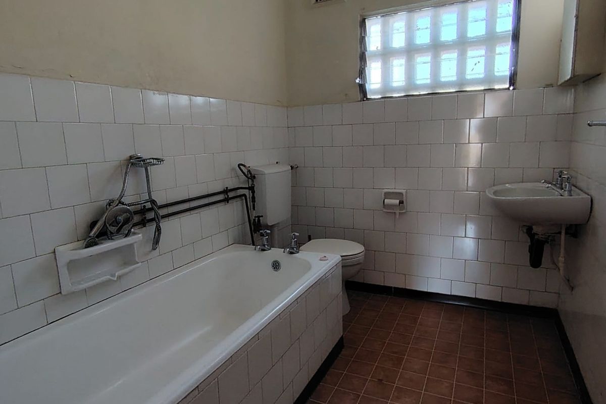 A dated bathroom featuring a bathtub, toilet, and wall-mounted basin with tiled finishes and exposed plumbing, offering significant potential for modernization.