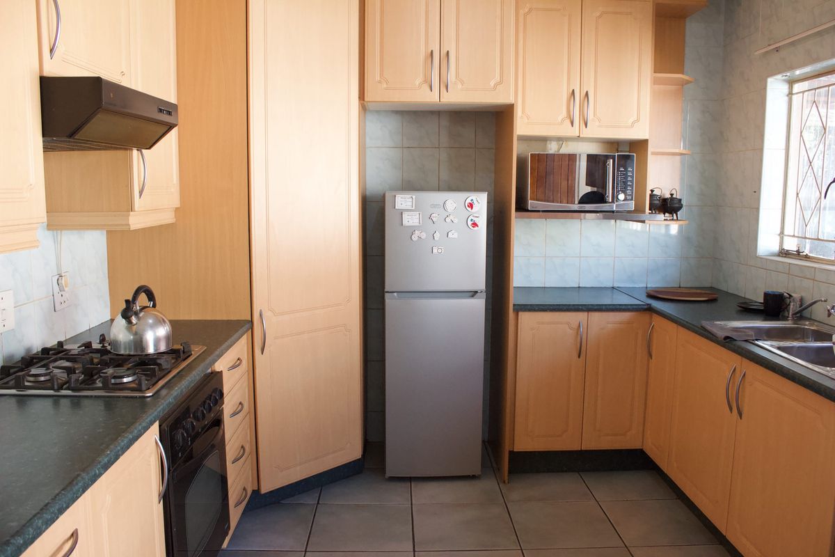 A functional kitchen featuring light wood-finish cabinetry, dark laminate countertops, a gas hob, and tiled flooring with a practical layout.