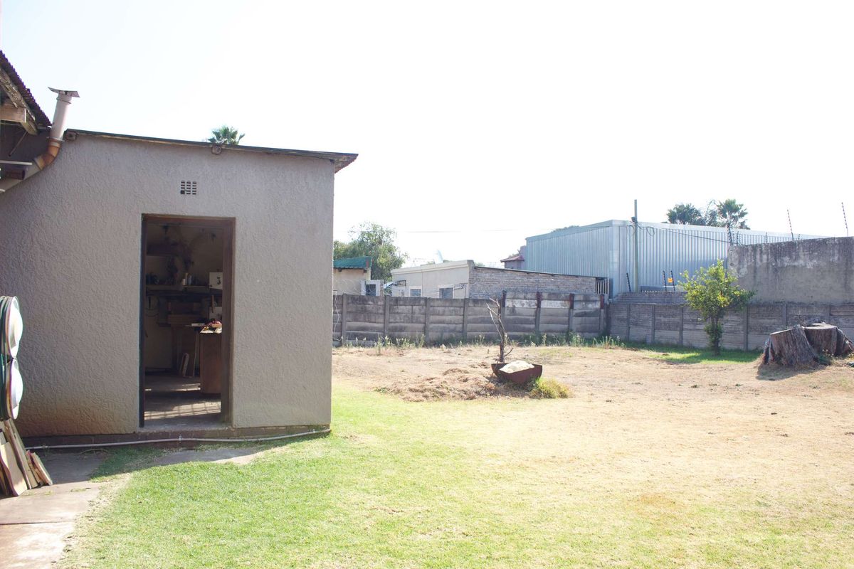 A view of the rear yard featuring a utility outbuilding, a large lawn area, and a precast concrete boundary wall.