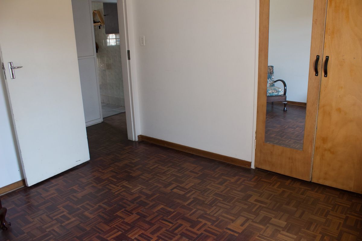 A bedroom featuring classic parquet flooring and a built-in wardrobe with a mirrored door, offering a clean and functional space.